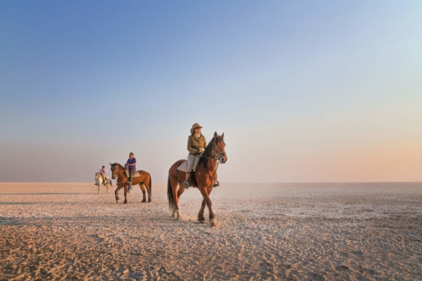 Horse riders on white salt pan with blue sky