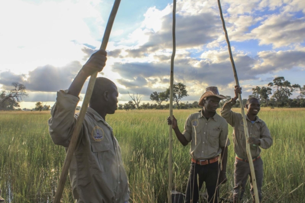 Three African men in safari outfits with long poles