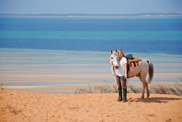Woman with white horse on dune overlooking ocean