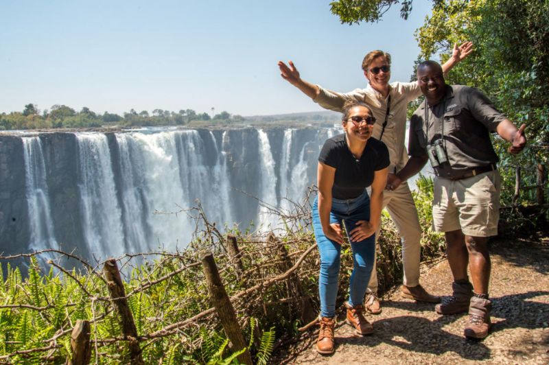 Smiling people in front of Victoria Falls waterfall
