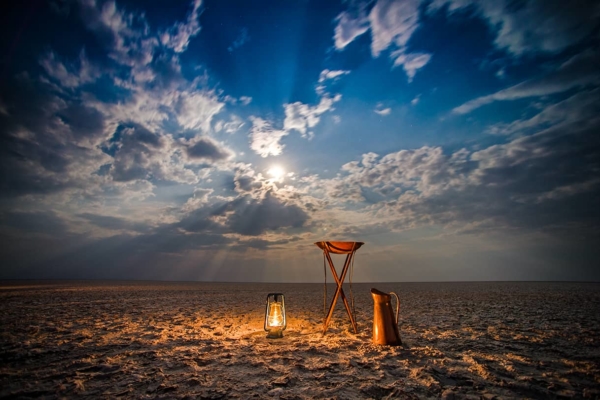 Glowing camp lantern and copper basin with dramatic cloudy sky and moon
