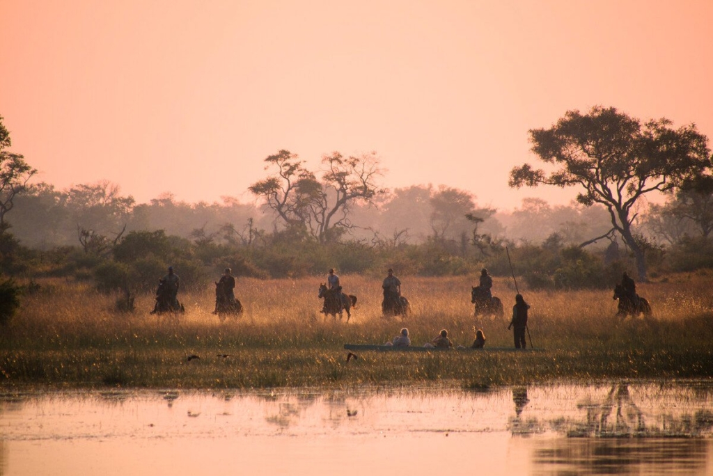 Horseback riders and Mokoro in the Okavango Delta in pink light