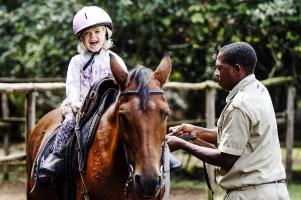 Child laughing on horse's back with man helping her ride