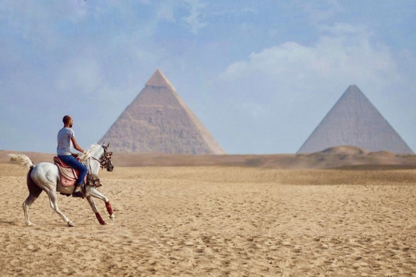 Man on white horse cantering in front of Egyptian Pyramids
