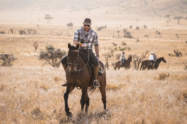 A man on a dark horse in the grasslands of Kenya
