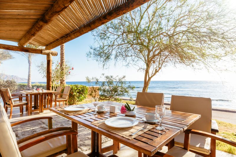 A cozy restaurant with wooden tables and chairs, offering ocean view.