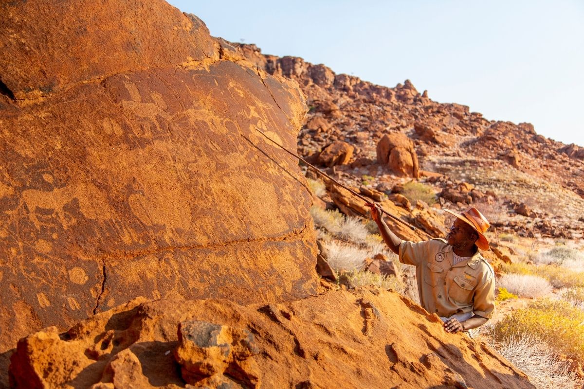 ranger showing ancient bushman rock art in damaraland, namibia