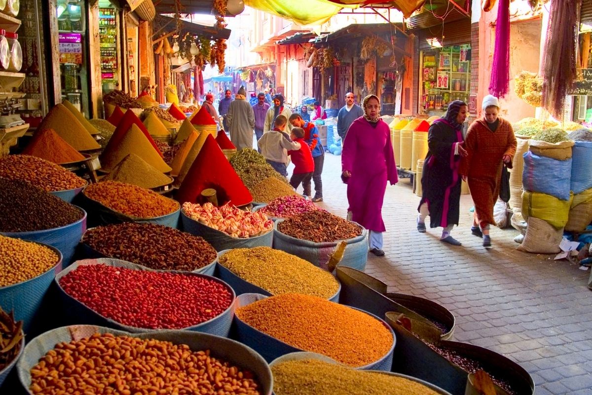 colourful spices at a local market in essaouira with people walking by in colourful clothing