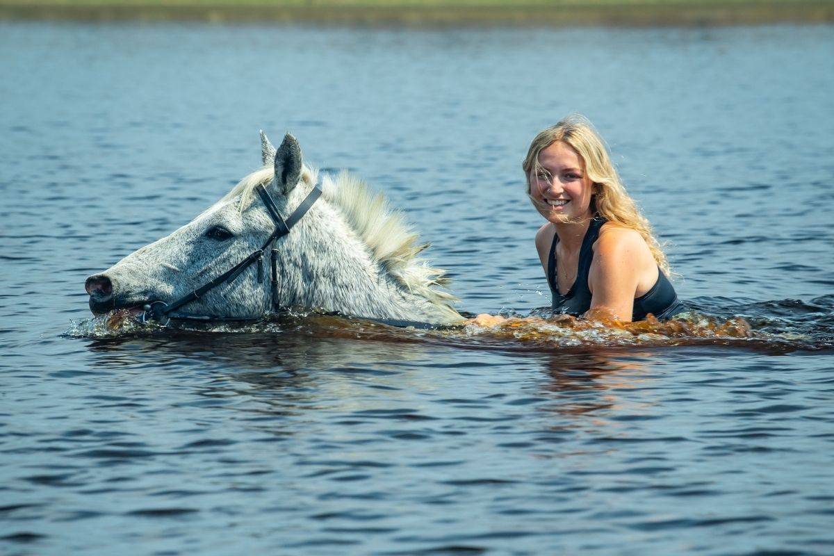 girl on grey horse swimming in a river