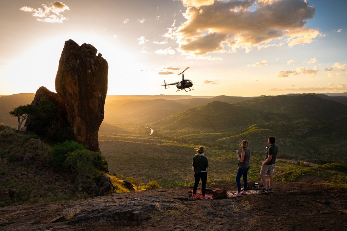 people having a picnic on a hill overlooking the valley with a helicopter flying nearby