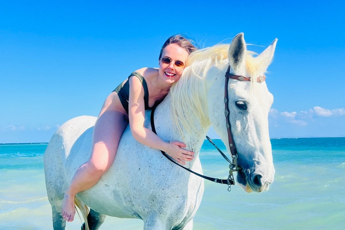 girl on grey horse hugging its neck with the ocean and white beach in the background in egypt