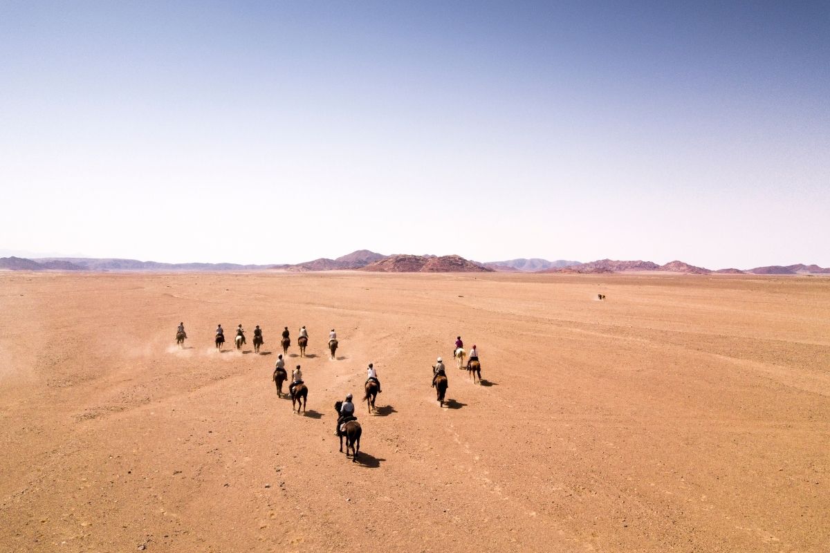horses and riders cantering across the open desert in namibia